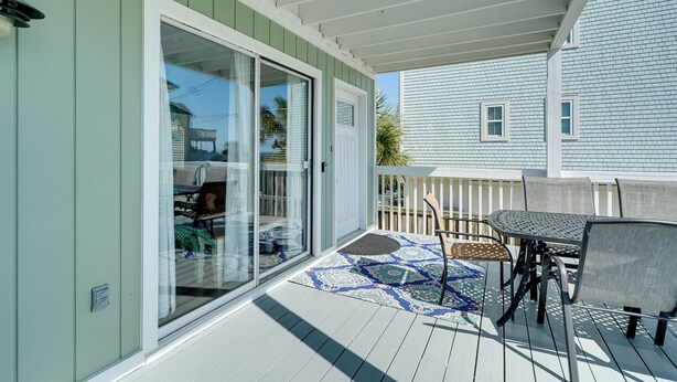 A covered patio with a table and chairs, a sliding glass door, and a patterned rug. - Condo w/ 2 Decks - Steps to Wrightsville Beach! (Wrightsville Beach)
