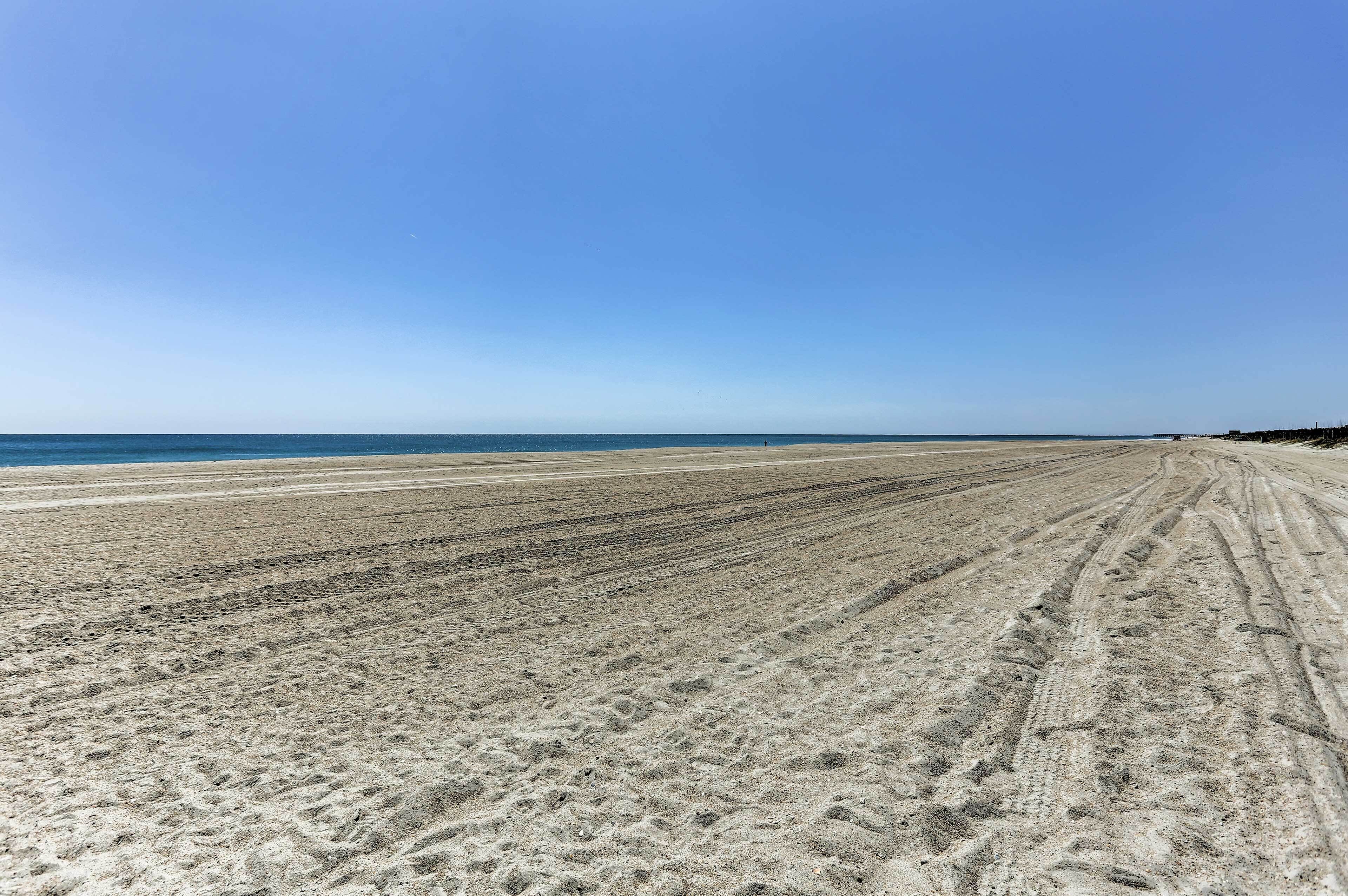 Ein weiter Sandstrand mit Radspuren und blauem, wolkenlosem Himmel.