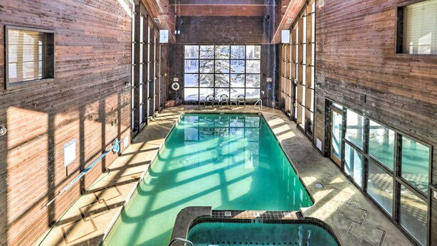 An indoor swimming pool with a view of a snowy landscape through large windows.