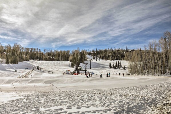A snowy ski slope with a ski lift, trees, and a clear sky.