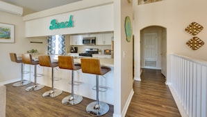 Una cocina moderna con barra, muebles blancos y un letrero de neón que dice "Beach".
