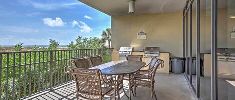 A balcony with a table and chairs, a grill, and a view of palm trees.