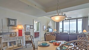 A dining area with a table set for four, a sofa, and a view of the sea through large windows.
