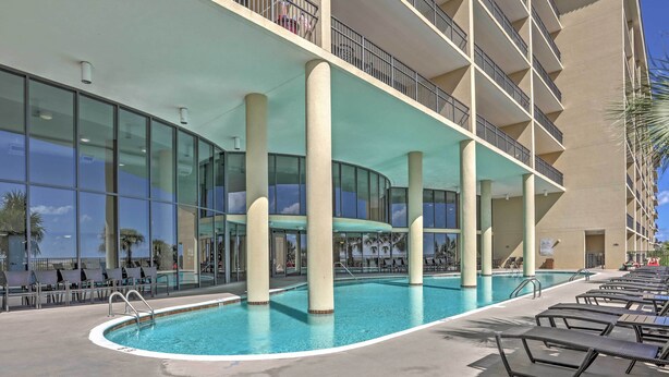 A hotel pool area with clear blue water, sun loungers, and a large glass facade.
