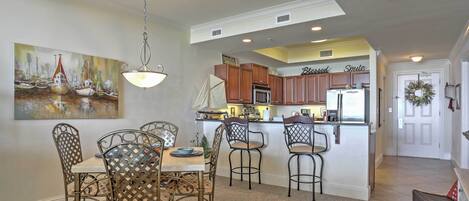 A dining area with a table and chairs, a kitchen with wooden cabinets, and a painting on the wall.