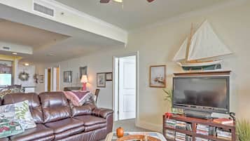 A living room with a brown leather sofa, a television, and a sailboat model on the wall.