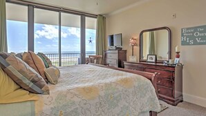 A bedroom with a large bed, a dresser, a television, and a view of the ocean.