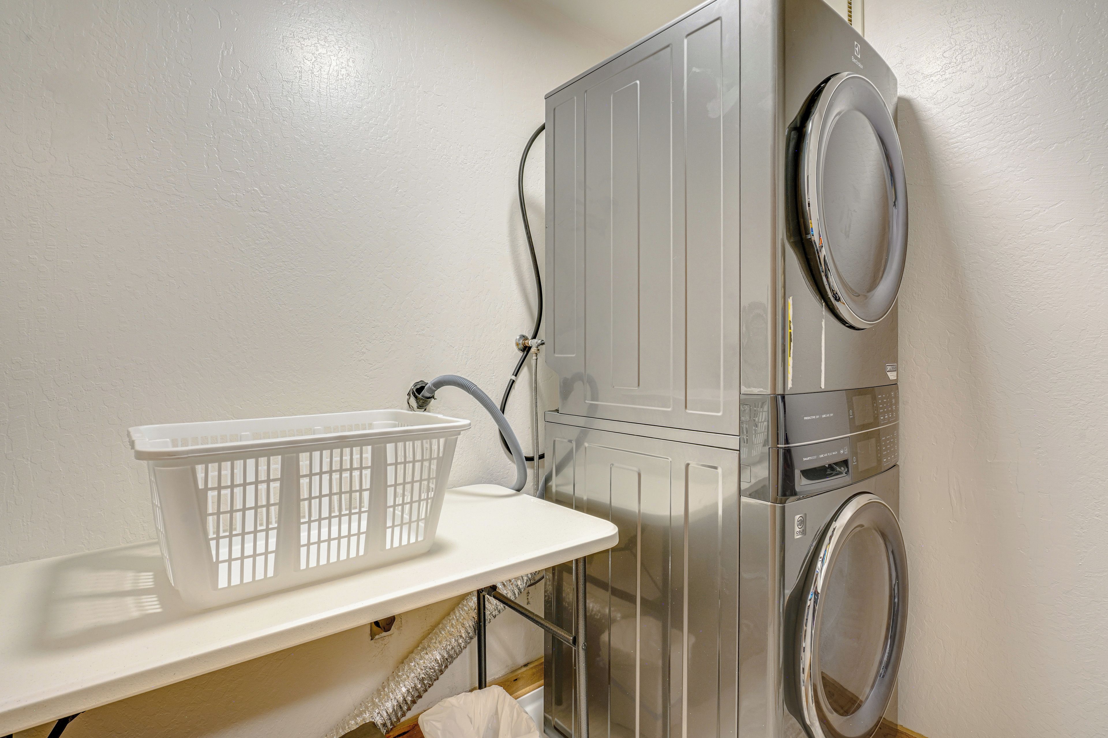 A laundry area with a washing machine, dryer, and a white laundry basket on a shelf.