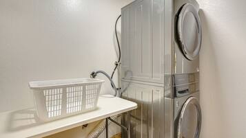 A laundry area with a washing machine, dryer, and a white laundry basket on a shelf.