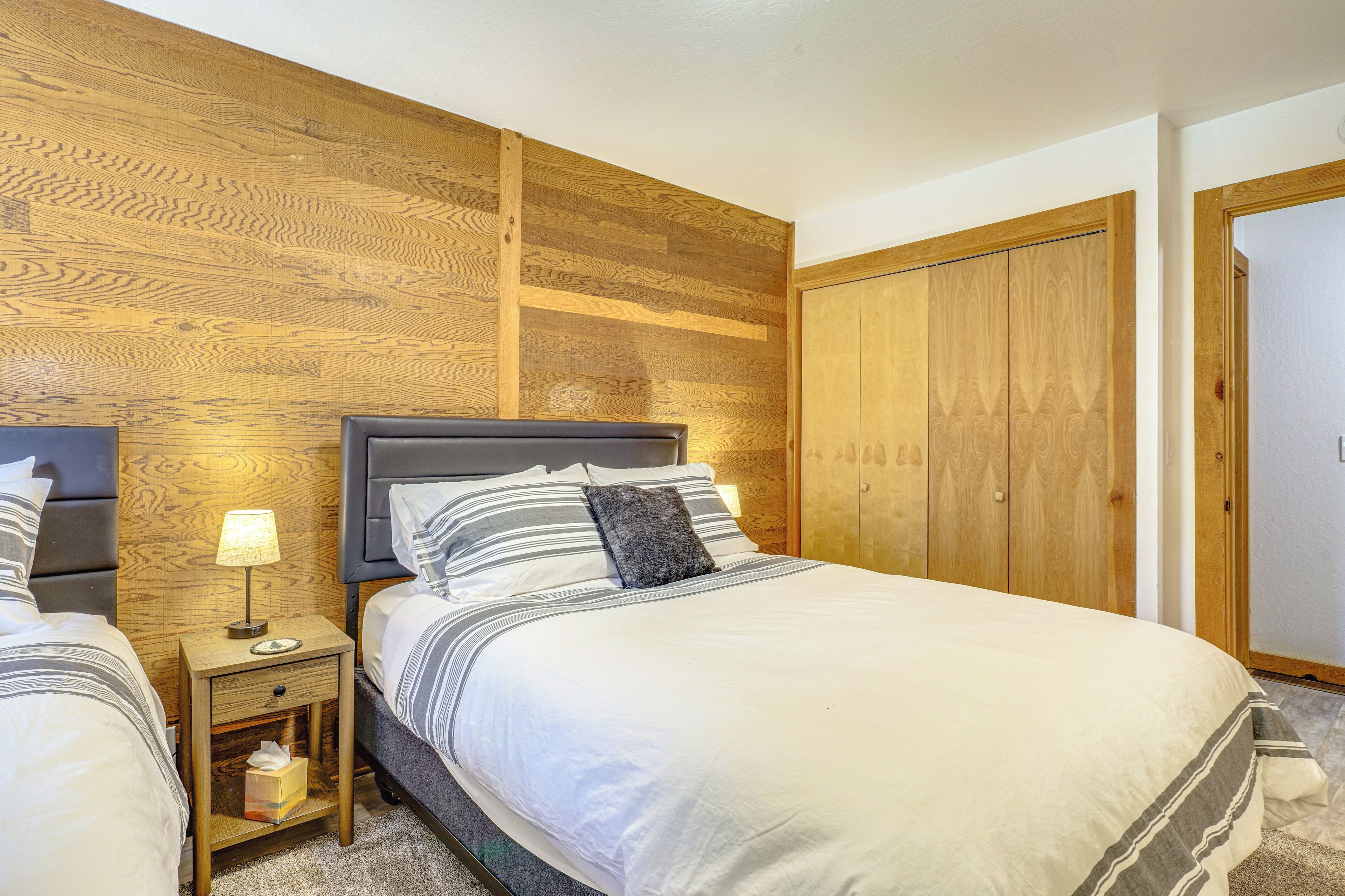 Un dormitorio con cabecera de madera, una mesita de noche con lámpara, cama con ropa de cama a rayas y un armario.
