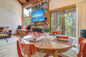 Zona pranzo con tavolo in legno, sedie e televisore a parete che mostra una scena di montagna innevata.