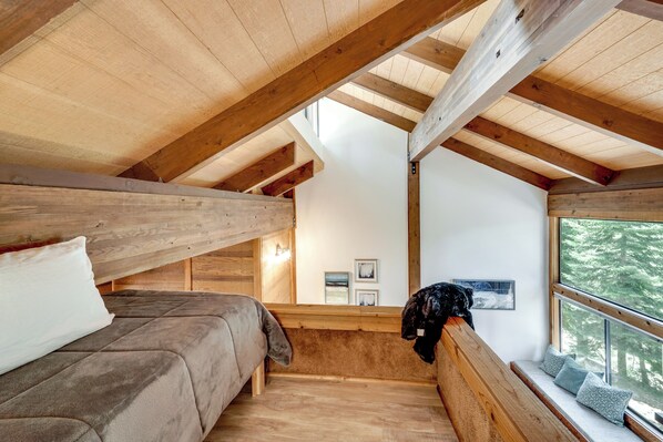 Una camera da letto mansardata accogliente con travi in legno, un letto a castello, una panchina finestrata e quadri appesi alle pareti.