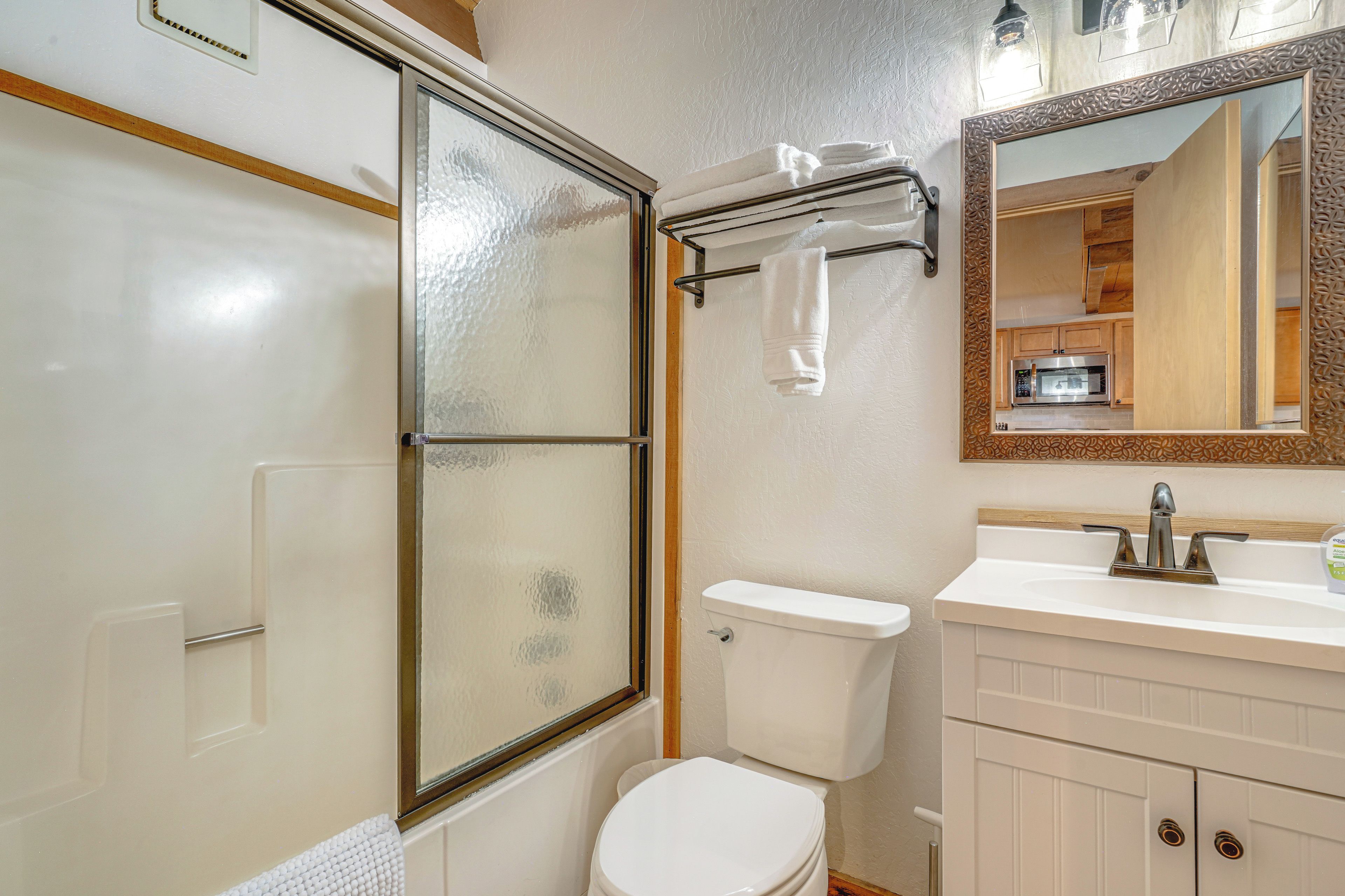 A bathroom with a glass shower enclosure, a toilet, a sink with a mirror, and a cabinet.