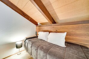 Una camera da letto con soffitto in legno, un letto con copriletto grigio e una lampada da comodino.