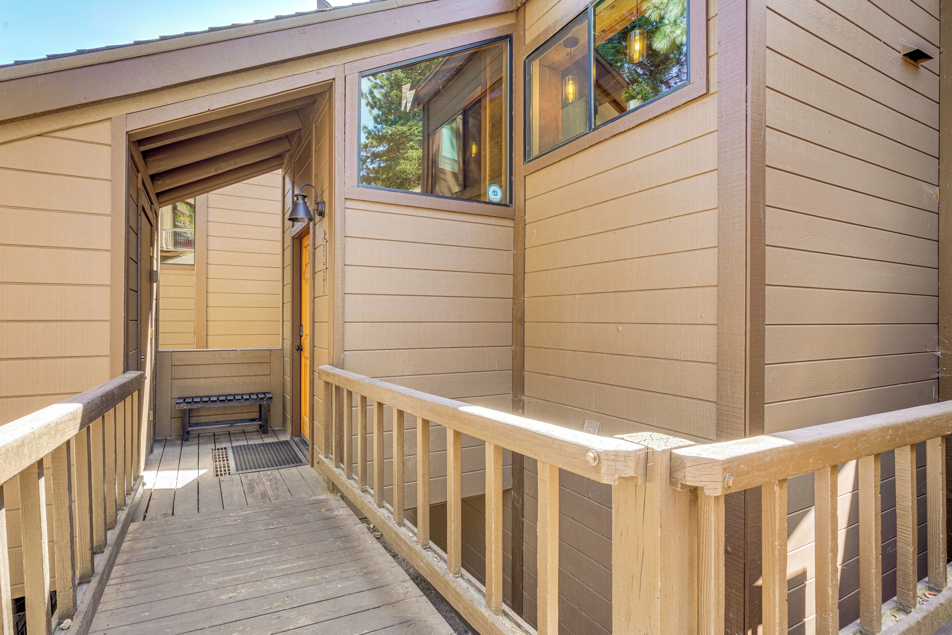 A wooden deck with a bench and a railing, leading to a building with large windows and a door.