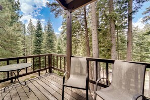 Une terrasse en bois avec une table et deux chaises, entourée de grands pins.