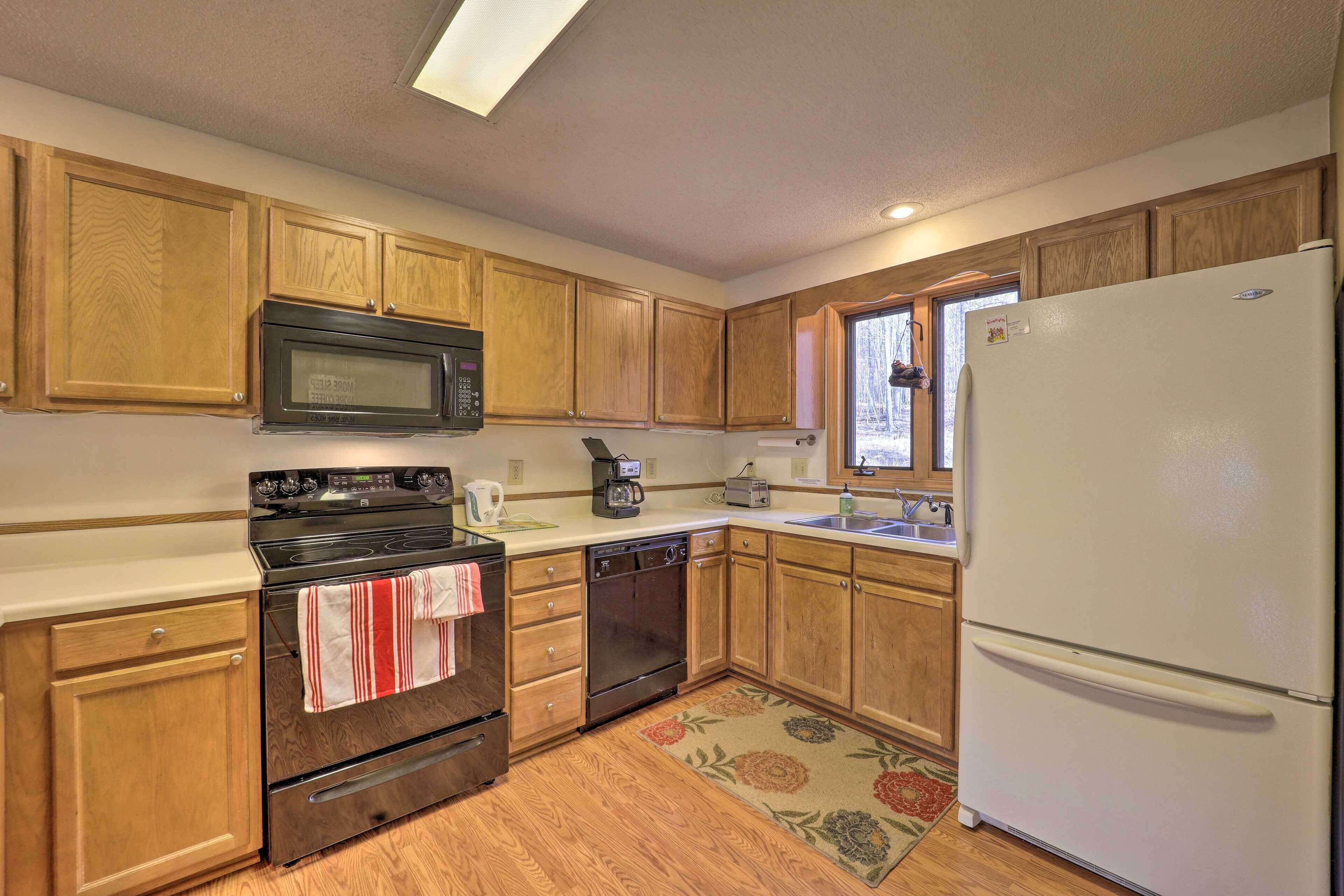 A kitchen with wooden cabinets, a microwave, stove, dishwasher, refrigerator, and a window.