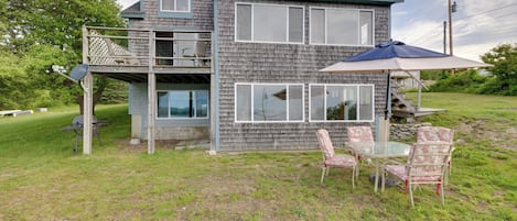 Ein zweistöckiges Haus mit einer Terrasse, Sitzgelegenheiten im Freien und einem Grill.