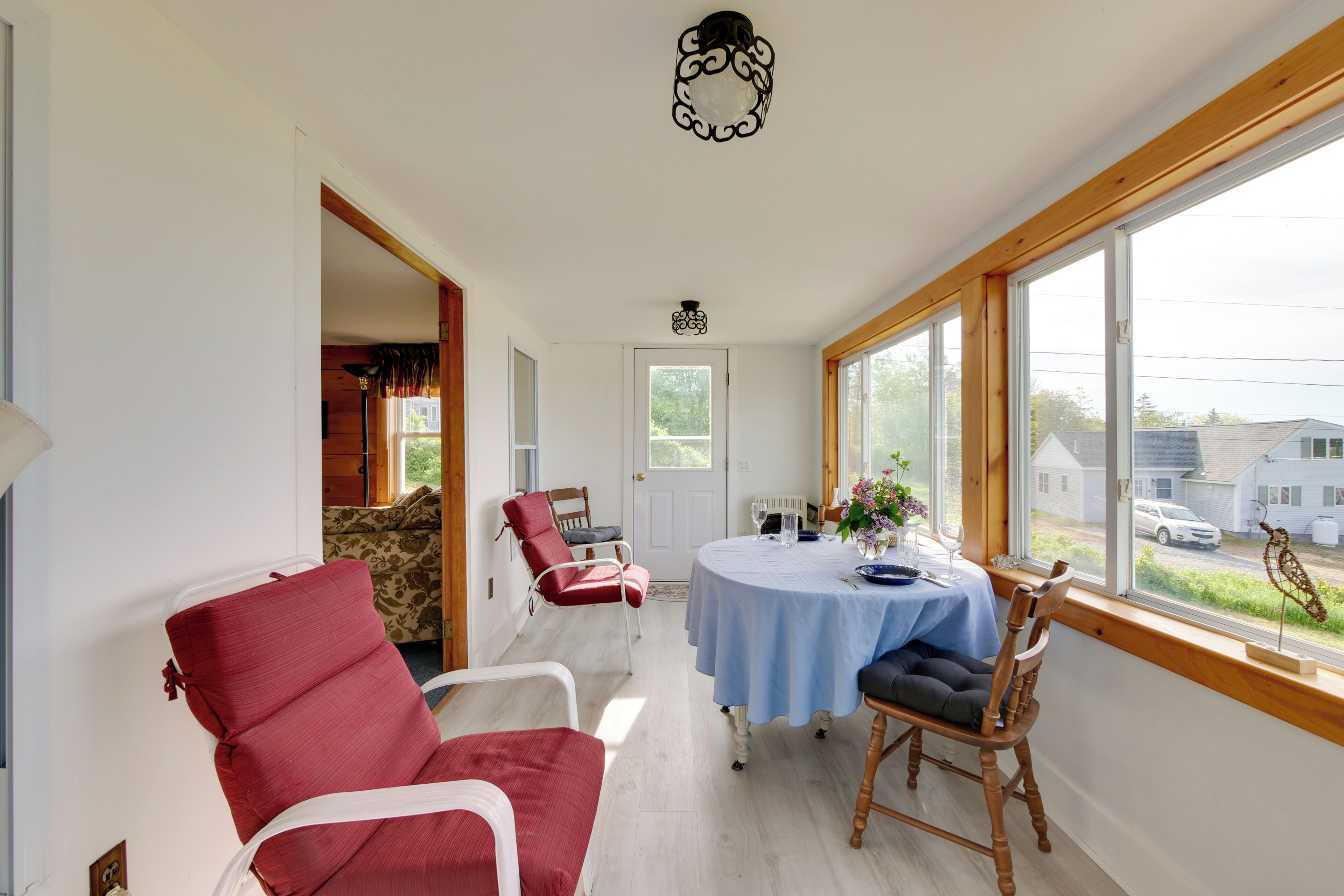 Habitació amb taula de dinar preparada per a dues persones, una butaca vermella, una cadira de fusta i vista exterior a través de grans finestres.