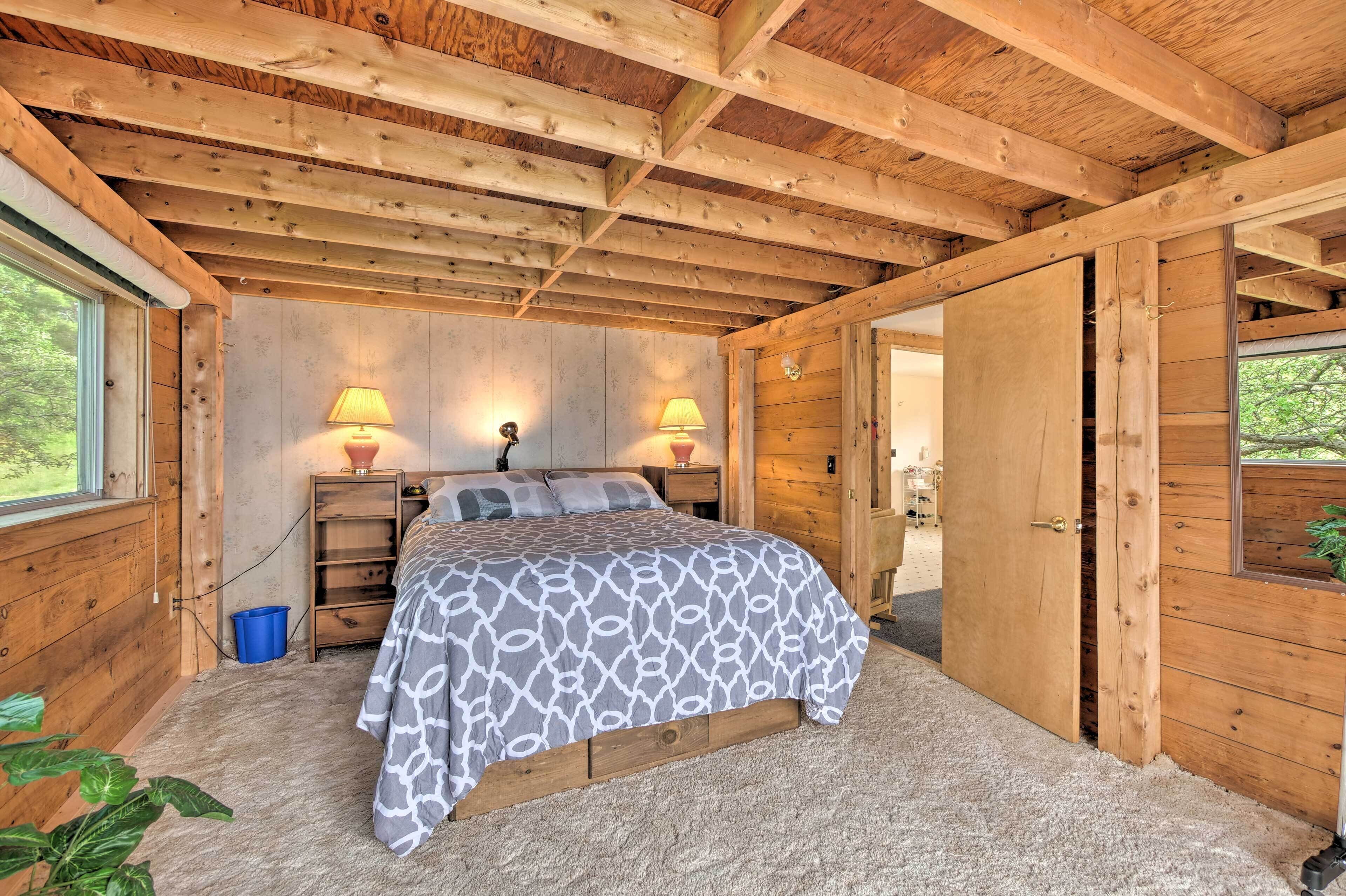 Ein Schlafzimmer einer Holzhütte mit einem Bett, zwei Nachttischlampen, einem Fenster und einer Tür.