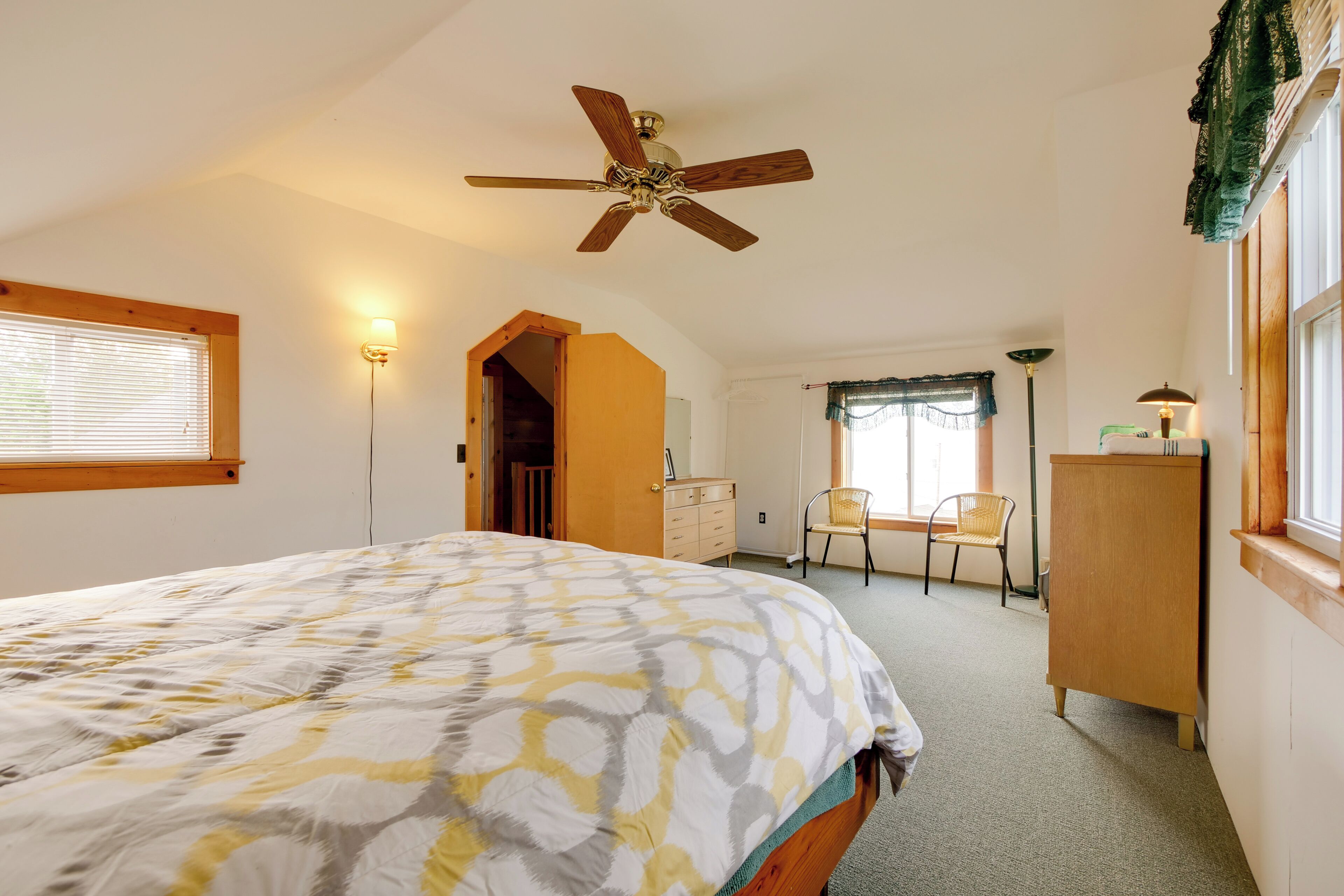 Een slaapkamer met een bed, plafondventilator, een dressoir, een stoel en een raam met jaloezieën.
