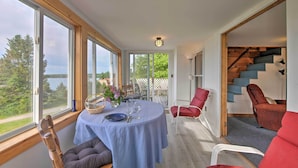 A dining area with a table set for two, large windows, and a staircase leading to an upper level. - Waterfront Cottage - 17 Mi to Acadia Ntnl Pk! (Ellsworth)