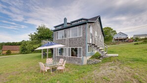 A two-story house with a covered patio area, a staircase leading to the upper floor, and a grassy yard. - Waterfront Cottage - 17 Mi to Acadia Ntnl Pk! (Ellsworth)