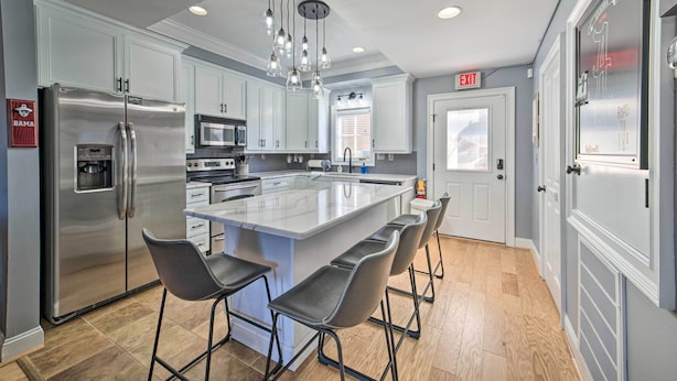 A modern kitchen with stainless steel appliances, a large island with bar stools, and a bright pendant light fixture. - Modern Retreat ~ 1/2 Mi to Bryant-denny Stadium (Tuscaloosa)