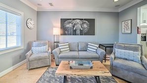 A living room with a grey sofa, two armchairs, a coffee table, a clock, and a large elephant painting on the wall. - Modern Retreat ~ 1/2 Mi to Bryant-denny Stadium (Tuscaloosa)
