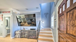 A modern living room with a large flat-screen TV, a staircase, and a wooden door. - Modern Retreat ~ 1/2 Mi to Bryant-denny Stadium (Tuscaloosa)