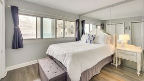 Une chambre à coucher avec un grand lit, une table de chevet avec une lampe, un banc et un miroir.