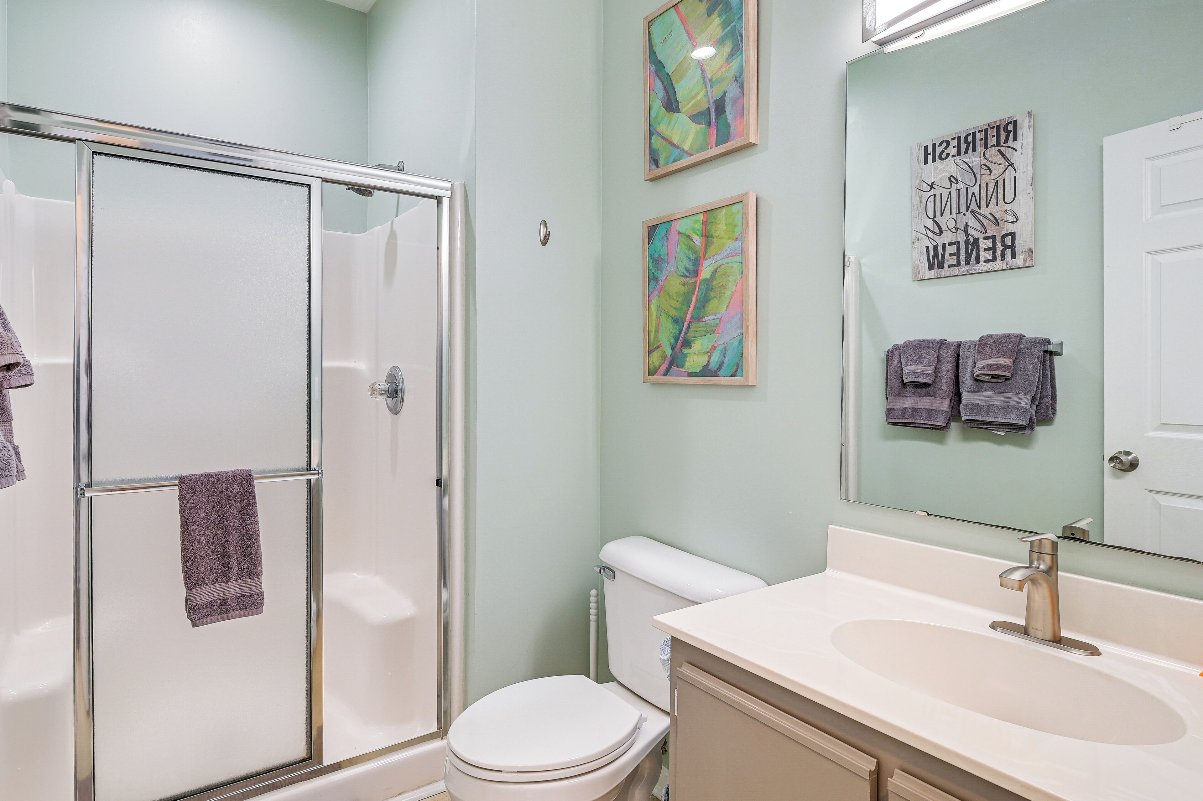 A bathroom with a glass shower enclosure, a white toilet, a sink with a mirror, and two towels hanging on the wall.