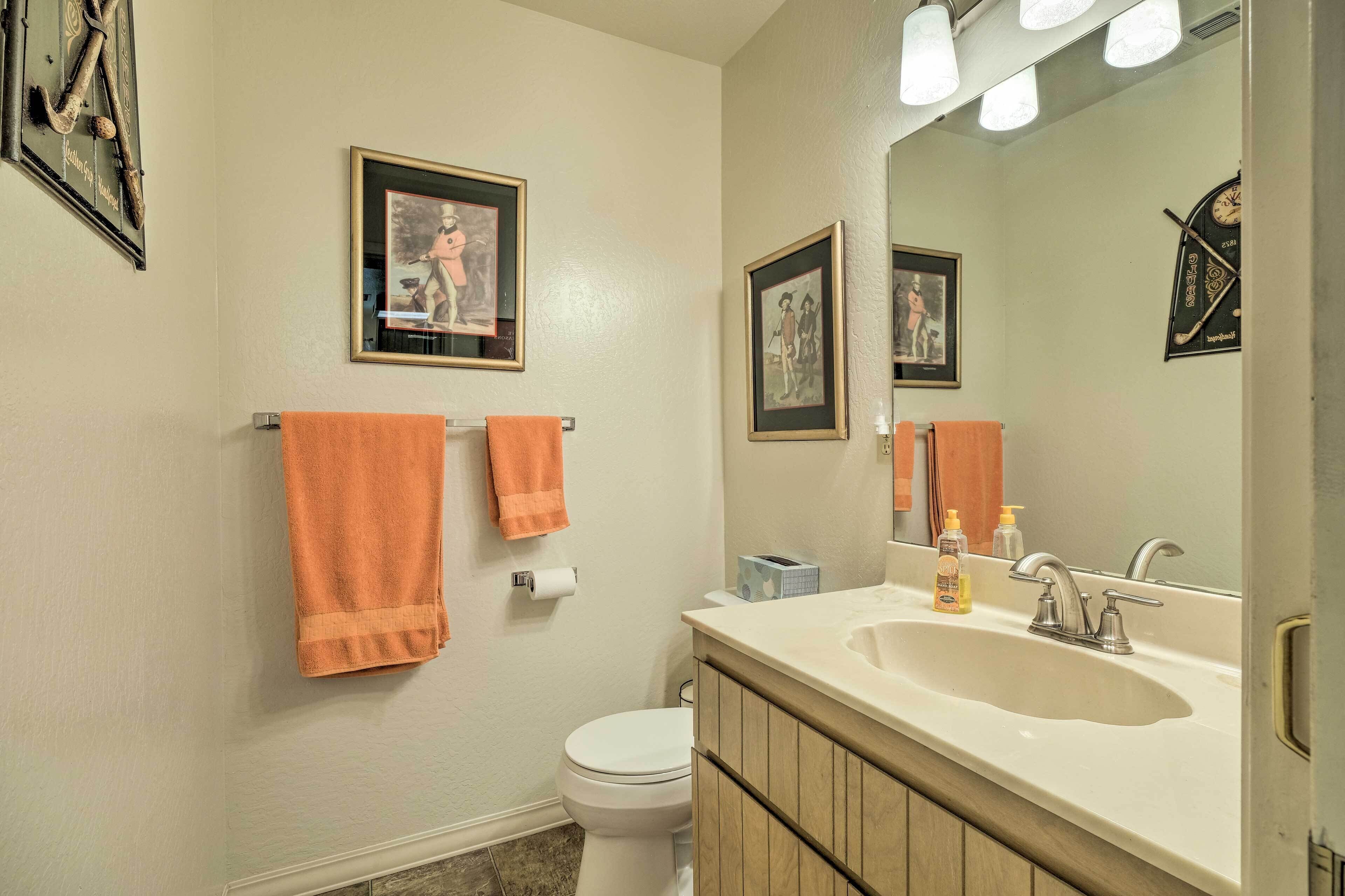 Un bagno con due asciugamani appesi al muro, un water, un lavandino con uno specchio e quadri incorniciati sopra lo specchio.