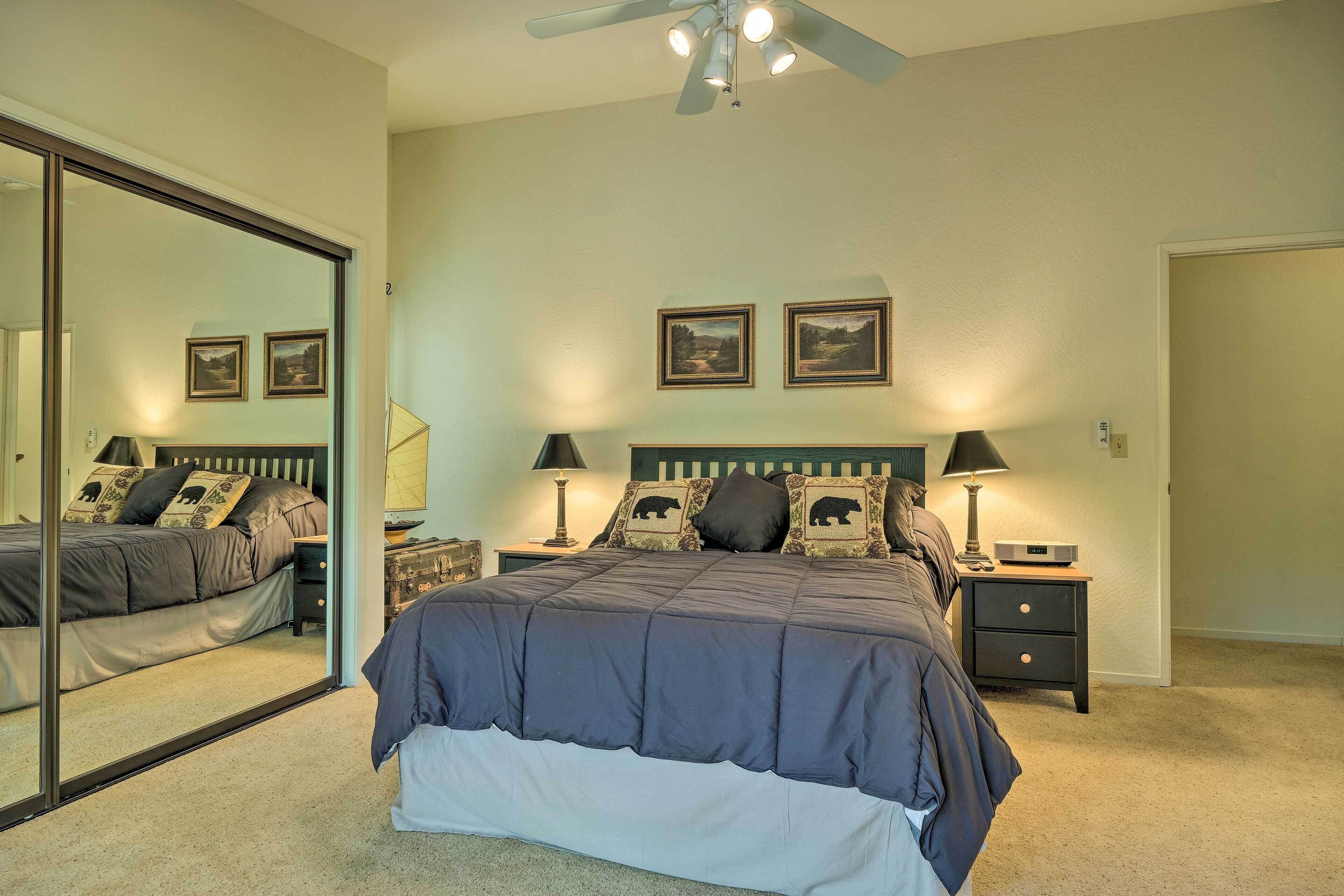 A bedroom with a large bed, two bedside tables with lamps, a ceiling fan, and two framed pictures on the wall.