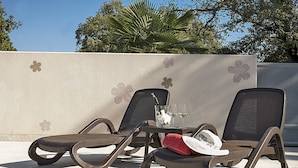 Dos sillones de descanso con una mesa en medio, una copa de vino blanco y una toalla roja sobre la mesa.