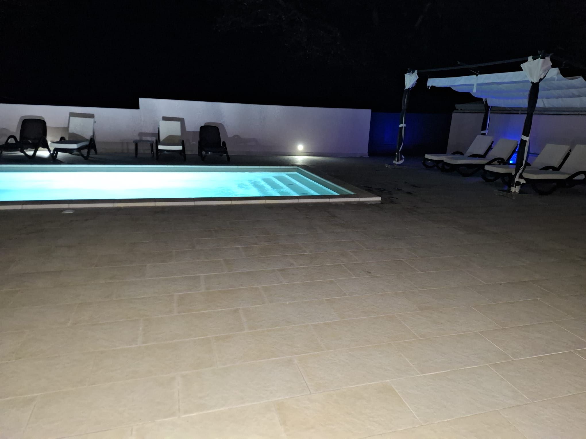 Una piscina all'aperto con lettini e una zona coperta.