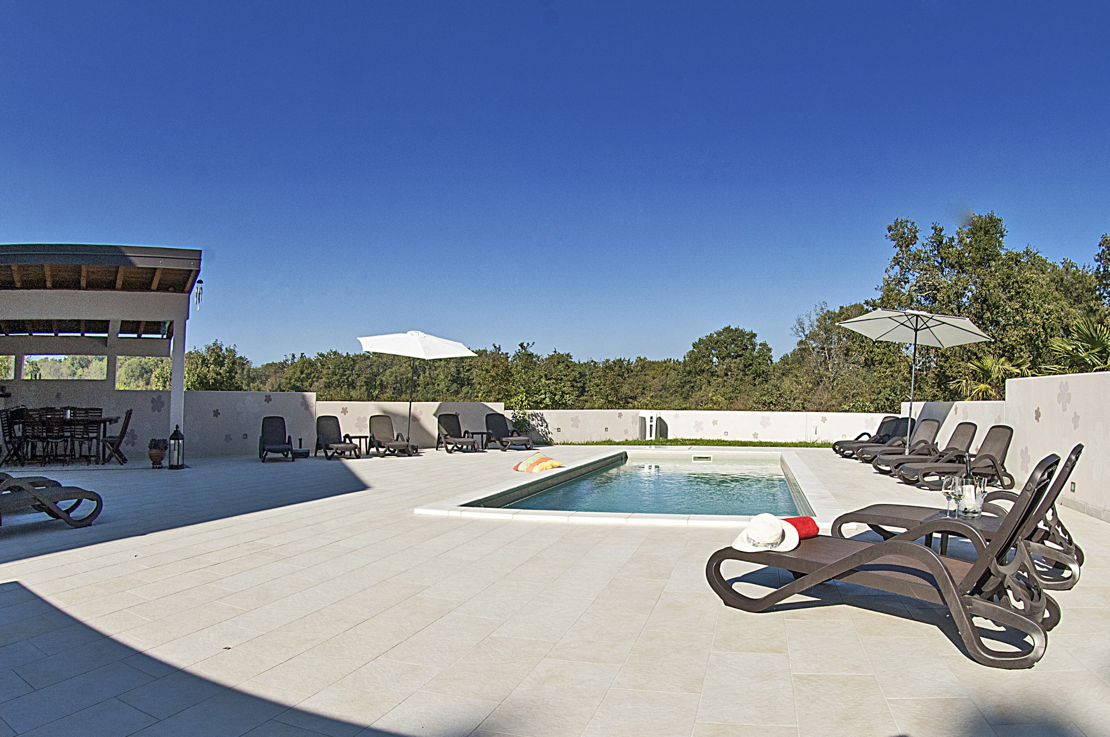 Un espace piscine comprenant des chaises longues, une petite piscine et un coin salon abrité.