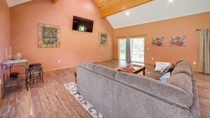 Un salon spacieux avec un grand canapé gris, un parquet en bois et un plafond haut avec des poutres apparentes.