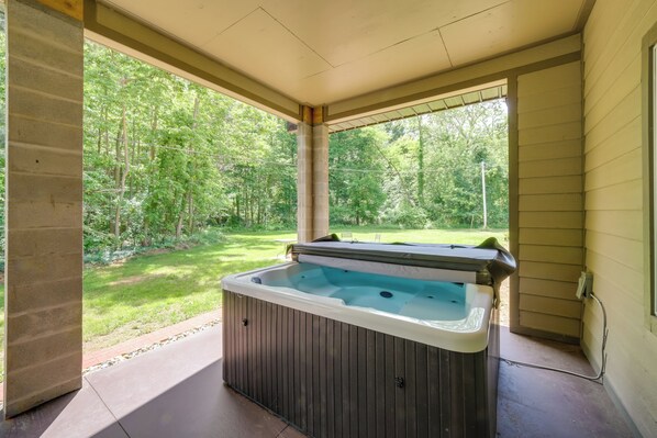 A hot tub in a covered outdoor area with a view of a forested yard.