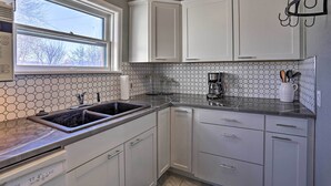 A kitchen with white cabinets, a hexagonal tile backsplash, and a window with a view of trees. - Rapid City Home w/ Patio by Canyon Lake Park! (Rapid City)