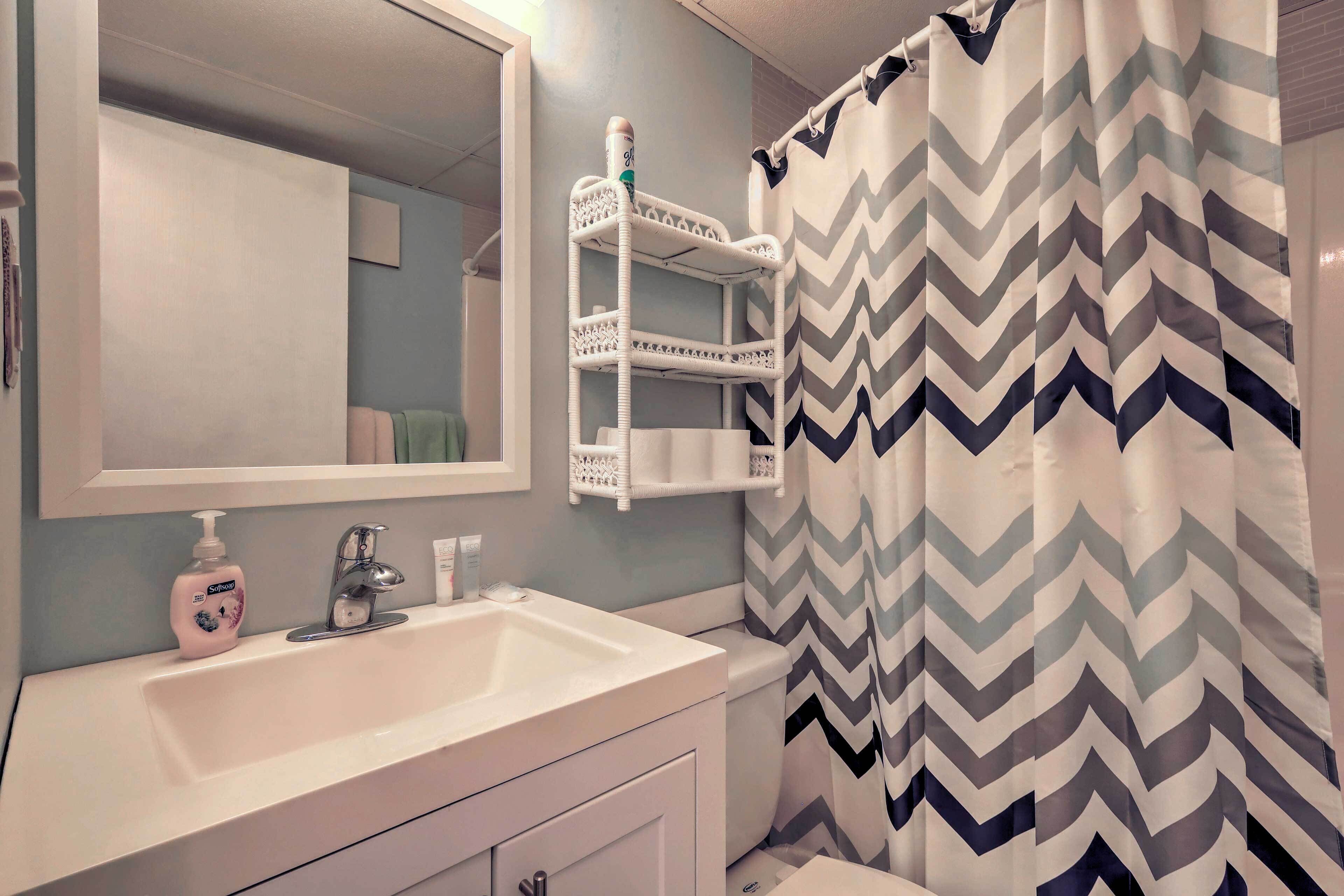 A bathroom with a white sink, a mirror, a toothbrush holder, and a shower curtain with a zigzag pattern.