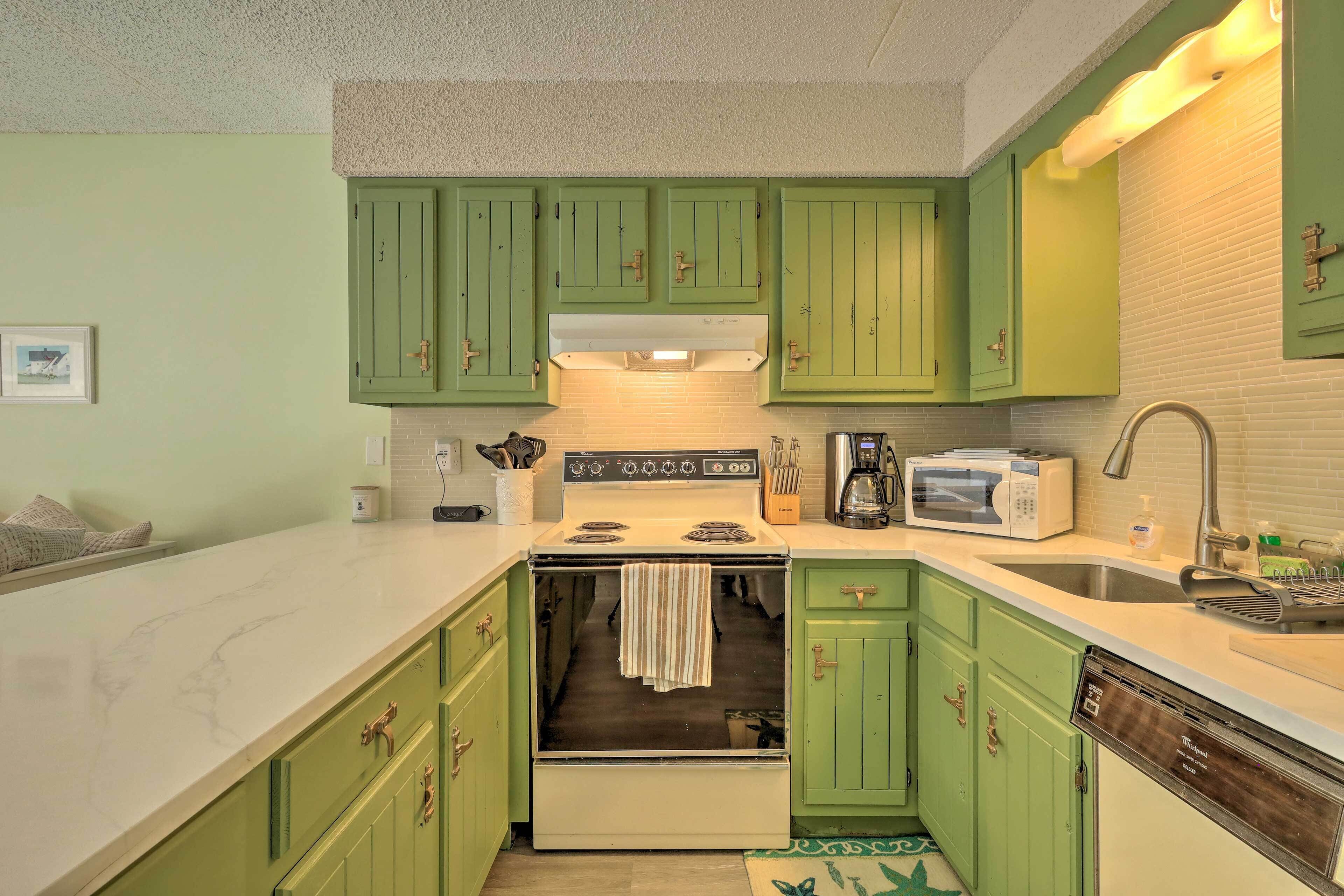 A kitchen with green cabinets, a white countertop, a stove, a microwave, and a dishwasher.