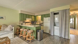 Una cocina compacta con gabinetes verdes, una isla central con taburetes, un refrigerador y un microondas.