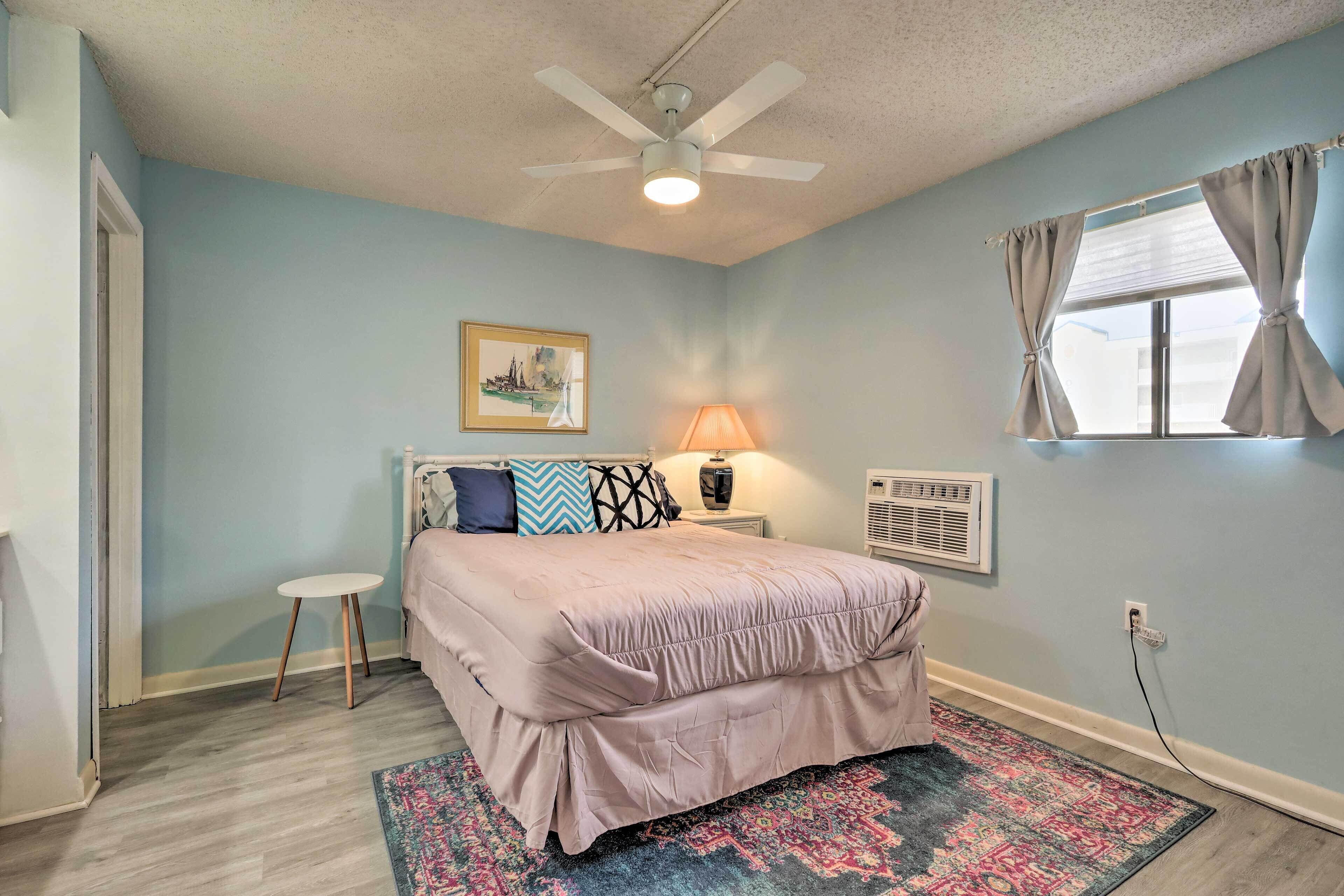 A bedroom with a bed, a standing lamp, a small table, a window with curtains, and a ceiling fan.