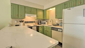 Una cocina con armarios verdes, un refrigerador blanco, un microondas y un fregadero.