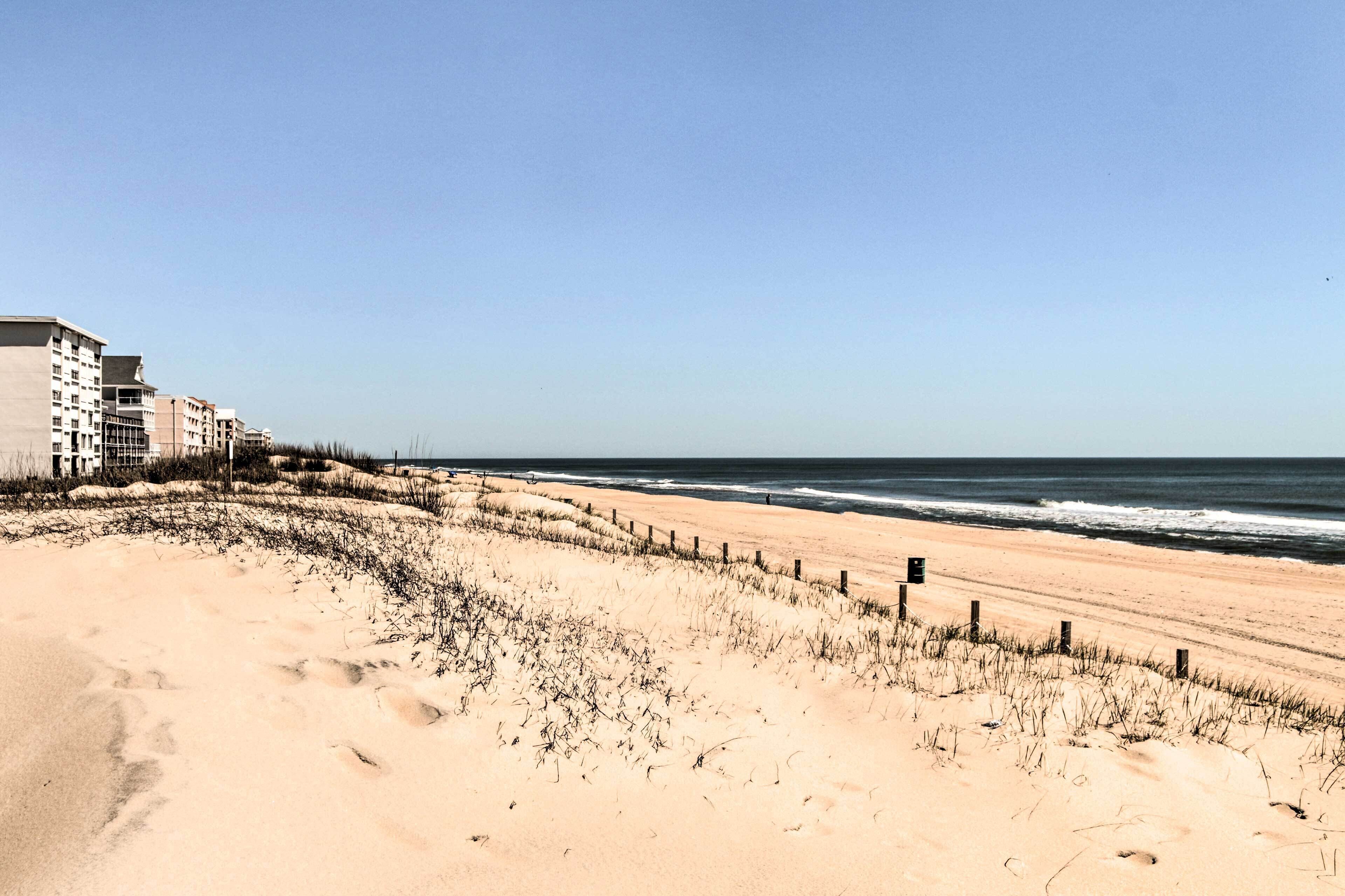A beach with a sandy shore, a wooden fence, and a building in the background.