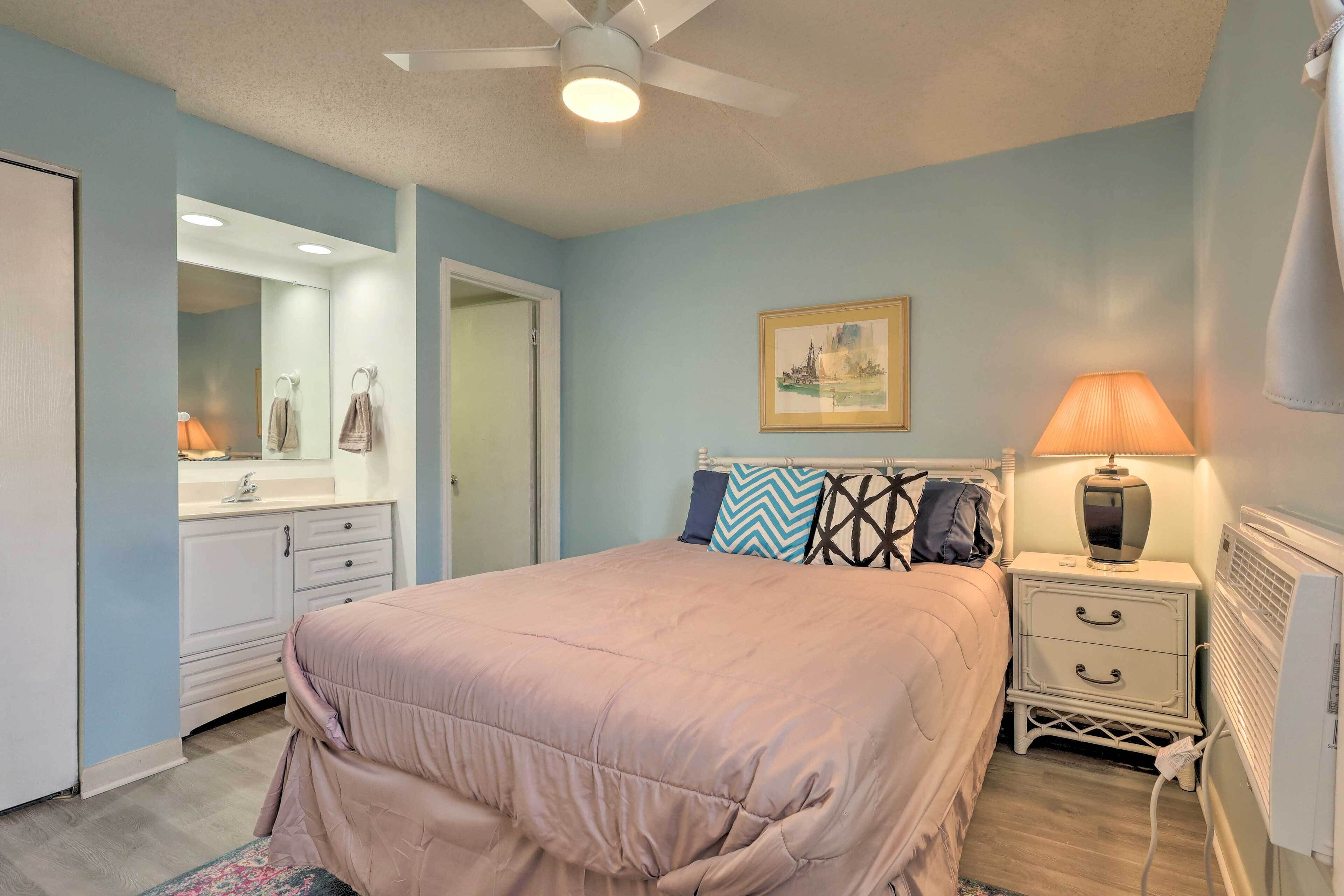 A bedroom with a bed, a nightstand with a lamp, a dresser, a mirror, and a painting on the wall.