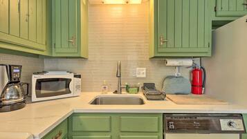 A kitchen with green cabinets, a microwave, a coffee maker, a sink, and a red fire extinguisher.