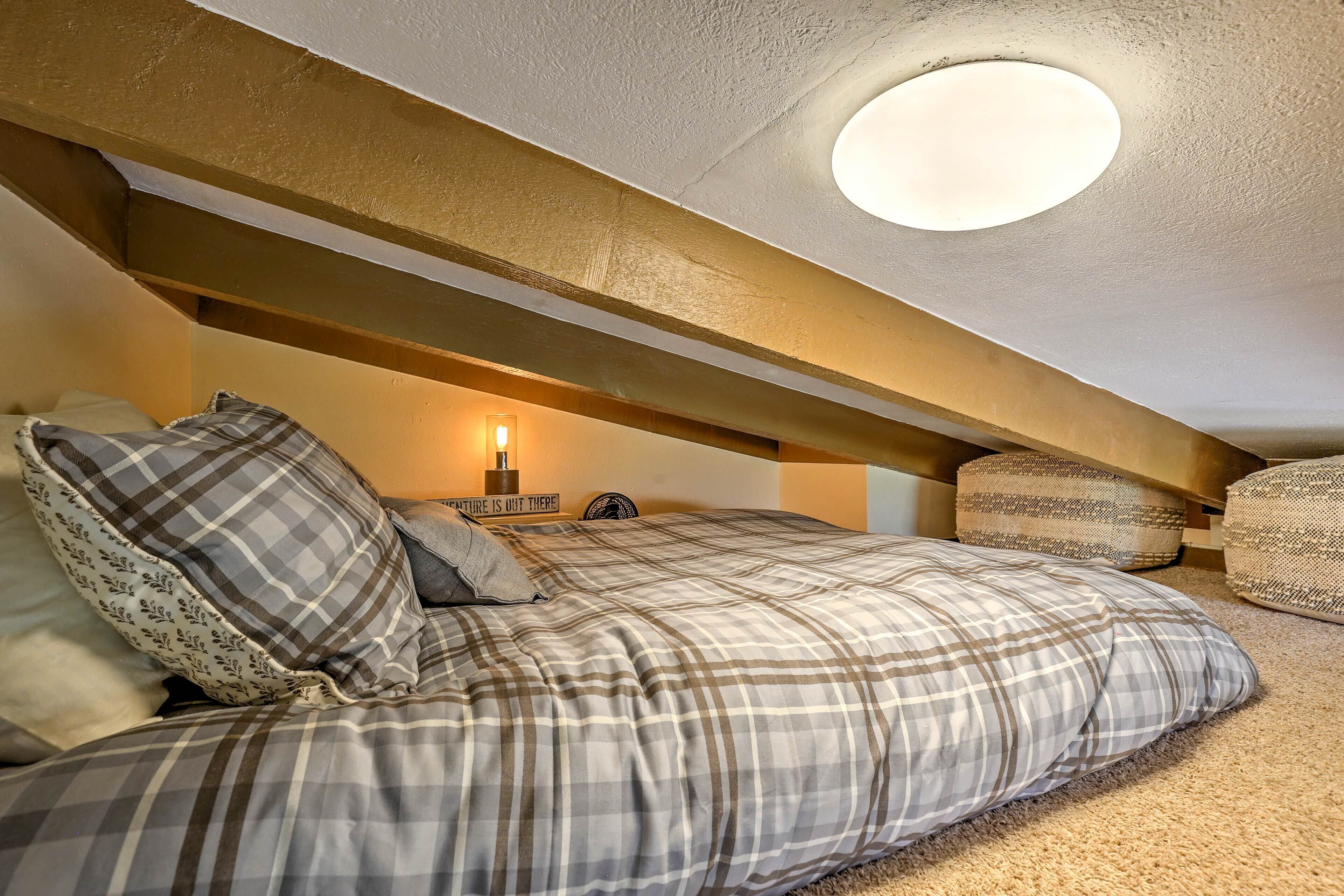 A cozy attic bedroom with a bed, pillows, and a wall-mounted lamp.