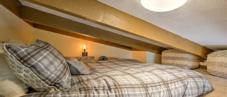 A cozy attic bedroom with a bed, pillows, and a wall-mounted lamp.